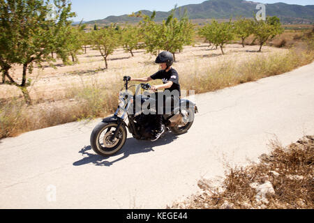 Junger Mann in Schwarz gekleidet auf einem schwarzen Motorrad Stockfoto