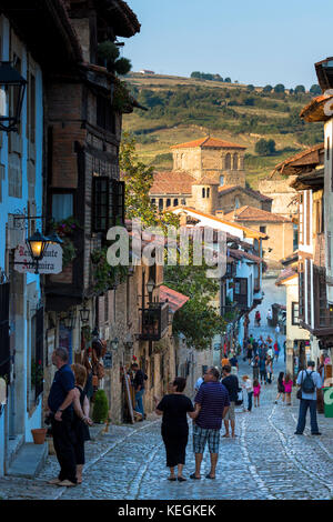 Touristen gehen vorbei an mittelalterlichen Gebäuden entlang der gepflasterten Straße Calle Del Kanton in Santillana del Mar, Kantabrien, Nordspanien Stockfoto