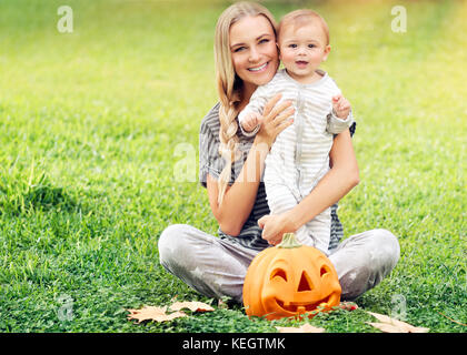 Mutter mit Baby Halloween genießen Urlaub im Freien, sitzen auf den frischen grünen Rasenfläche, traditionelle festliche Dekoration, Familie Spaß Stockfoto