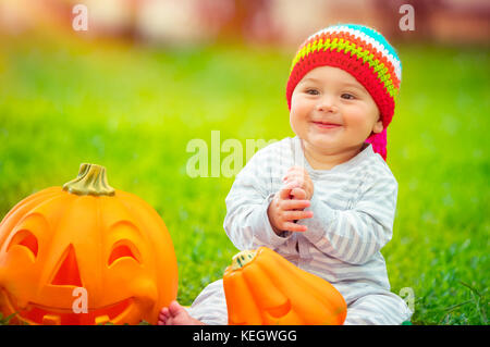 Süße kleine baby boy trug Lustig bunten Hut, Spielen mit zwei schöne geschnitzte Kürbisse, traditionelle halloween Symbol, Spaß an sonnigen autumna Stockfoto