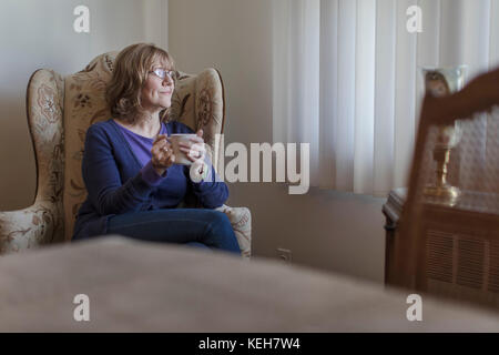 Kaukasische Frau sitzt im Stuhl in der Nähe der Fenster Kaffee trinken Stockfoto