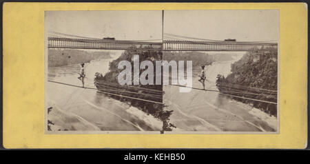 Foto von Samuel Mason, das einen Mann zeigt, der an einem Draht hängt, der den Fluss in der Nähe der Niagarafälle überquert, und zeigt eine Drahtseilvorführung aus dem 19. Jahrhundert. Stockfoto