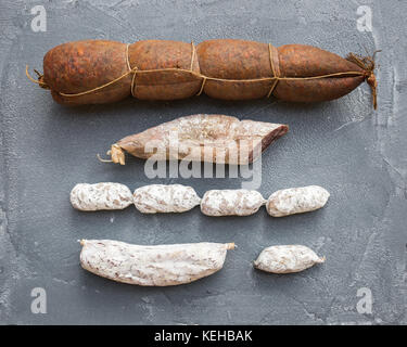 Italienische Salami Würstchen verschiedener Arten über eine grobe grauer Beton strukturierten Hintergrund, Ansicht von oben, horizontal Stockfoto