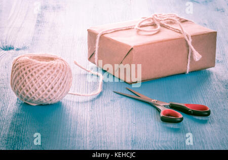 Geschenkbox hausgemachte, im klassischen braunes Papier, Ball von string und die Schere auf einer blauen Tabelle verpackt Stockfoto