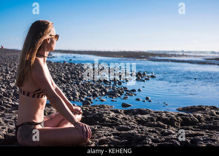 Kaukasische Frau sitzt am Strand in Bikini Stockfoto