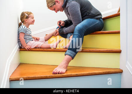 Kaukasische Mutter Malerei Zehennägel der Tochter auf mehrfarbigen Treppe Stockfoto