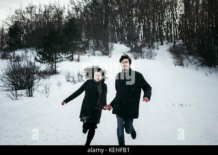 Kaukasisches Paar läuft im Winter aus dem Wald Stockfoto