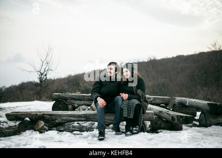 Kaukasisches Paar sitzt im Winter auf Holzstämmen Stockfoto