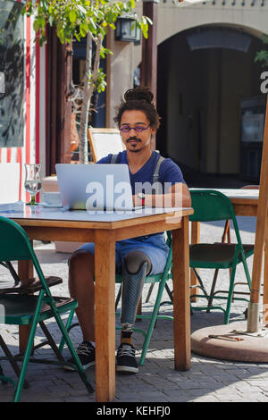 Gemischter Rennmensch mit Beinprothese mit Laptop im Straßencafé Stockfoto