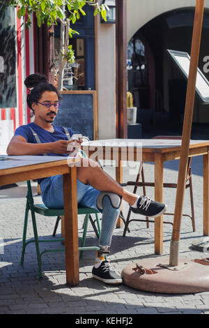 Gemischter Renner mit prothetischen Beintexten auf dem Handy im Bürgersteig-Café Stockfoto