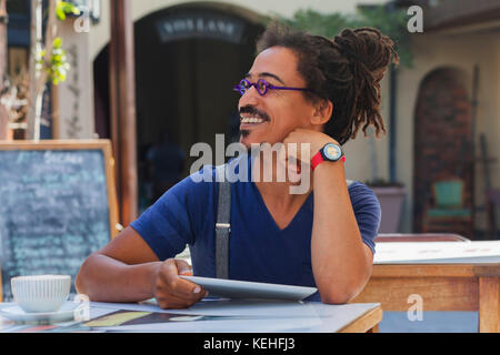 Lächelnder gemischter Rennmensch mit digitalem Tablet im Straßencafé Stockfoto