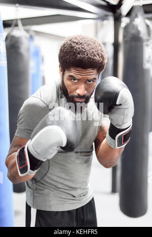 Portrait des schwarzen Mannes mit Boxhandschuhen in der Turnhalle Stockfoto