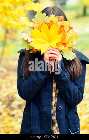 Mädchen verbirgt ihr Gesicht hinter gelben Blätter im Herbst, Bouquet, Herbst Stockfoto