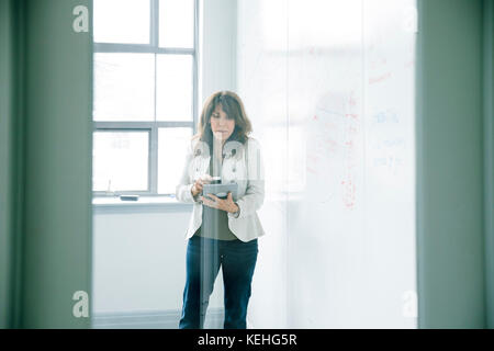 Kaukasische Geschäftsfrau hält digitales Tablet in der Nähe von Whiteboard Stockfoto