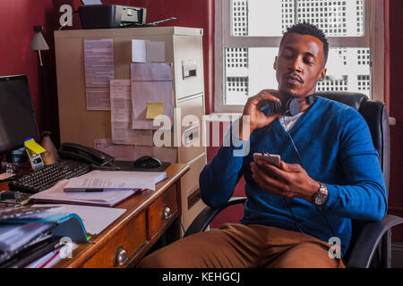 Schwarzer Mann liest Handy und hält Kopfhörer Stockfoto
