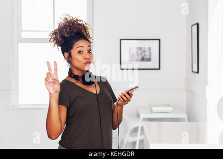 Gemischte Rasse Frau hält Handy gestikulierenden Frieden Stockfoto