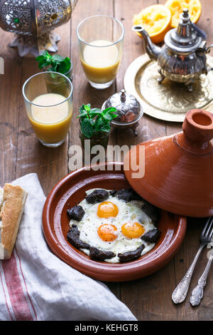 Sunnyside Eier in einer tajine Gericht mit Rindfleisch gekocht, marokkanisches Frühstück mit Saft und Pfefferminztee. Stockfoto