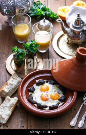 Sunnyside Eier in einer tajine Gericht mit Rindfleisch gekocht, marokkanisches Frühstück mit Saft und Pfefferminztee. Stockfoto