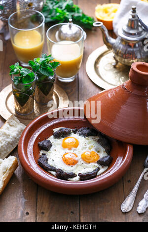 Sunnyside Eier in einer tajine Gericht mit Rindfleisch gekocht, marokkanisches Frühstück mit Saft und Pfefferminztee. Stockfoto