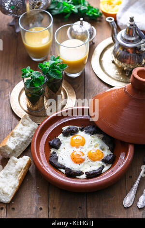 Sunnyside Eier in einer tajine Gericht mit Rindfleisch gekocht, marokkanisches Frühstück mit Saft und Pfefferminztee. Stockfoto