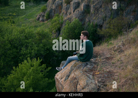 Kaukasischer Mann auf einem Felsen sitzend und die Landschaft bewundernd Stockfoto