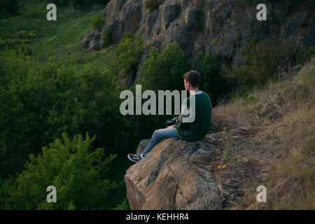 Kaukasischer Mann auf einem Felsen sitzend und die Landschaft bewundernd Stockfoto