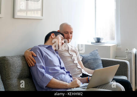 Kaukasische Männer umarmen auf dem Sofa und mit Laptop Stockfoto