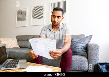 Gemischter Renner sitzt auf dem Sofa und liest Papierkram Stockfoto