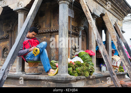 Banana leaf Verkäufer Schutz gegen den Regen unter einem alten Gebäude, das nach dem Erdbeben von 2015 wiederhergestellt wird. Kathmandu, Nepal. Stockfoto