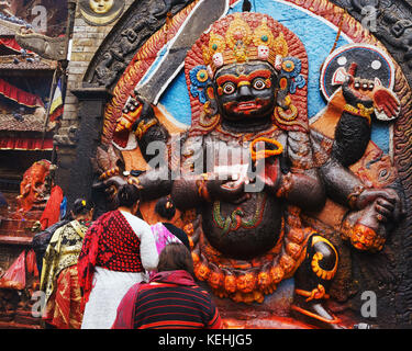 Hinduistische Frauen holen Angebote beim Denkmal der Schwarzen Bhairab, eine furchteinflößende Darstellung von Shiva. Durbar Square, Khatmandu, Nepal. Stockfoto