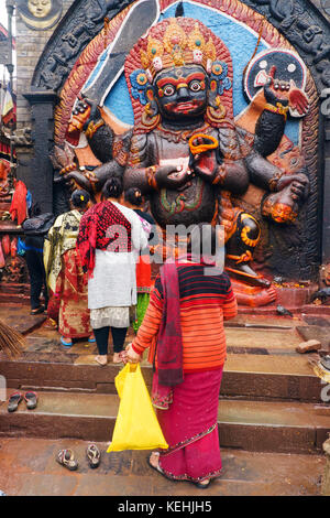 Hinduistische Frauen holen Angebote beim Denkmal der Schwarzen Bhairab, eine furchteinflößende Darstellung von Shiva. Durbar Square, Khatmandu, Nepal. Stockfoto