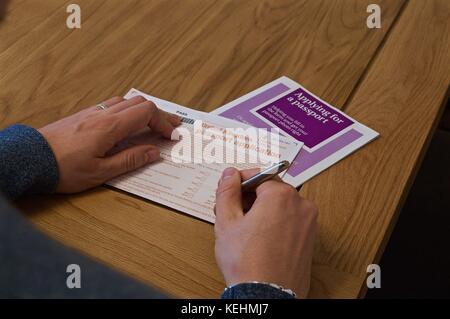 Blick auf die Hände des Menschen Ausfüllen britischen Reisepass Antragsformular auf Tabelle mit anweisende Broschüre Stockfoto