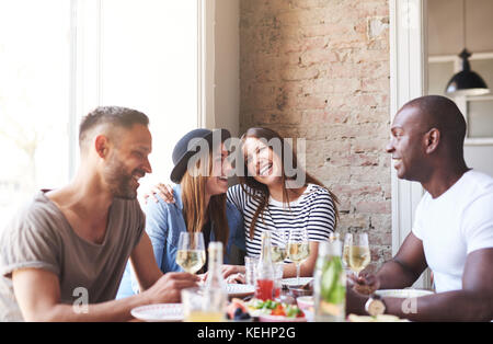 Eine Gruppe von vier Jugendlichen Abendessen im Restaurant und im Gespräch mit einem Lächeln. Stockfoto