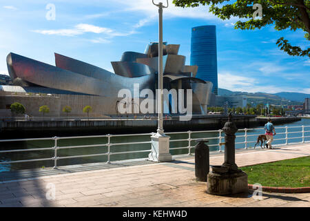 Mann, der Hund geht, hat am Guggenheim Museum des Architekten Frank Gehry über den Fluss Nervion in Bilbao, Baskenland, Spanien, vorbeigelaufen Stockfoto