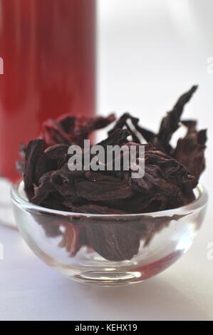 Getrocknete Hibiscus Blüten in eine Glasschüssel und Hibiskus Infusion Tee im Hintergrund. tiefes Rot pflanzliche heißen Getränk. isoliert auf weißem Stockfoto