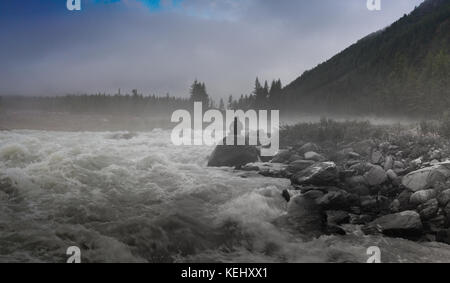 Die Silhouette eines Mannes, der in der Finsternis der Nacht Fotografie. dichter Nebel über dem Fluss Stockfoto