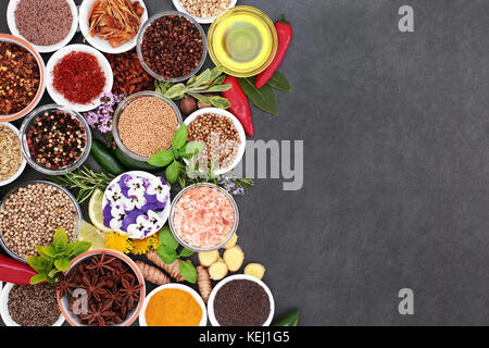 Frische und getrocknete Kräuter und Gewürze Auswahl mit essbaren Blüten und Olivenöl bildet eine abstrakte Grenze auf schiefer Hintergrund. Stockfoto