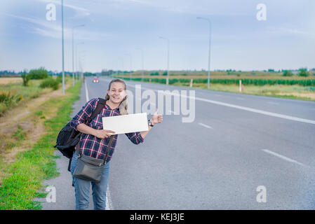 Lächelnde Frau per Anhalter auf der Straße hält ein Blank Board. Konzept: die Welt, Euro, urlaub reisen, Menschen, Urlaub. Stockfoto