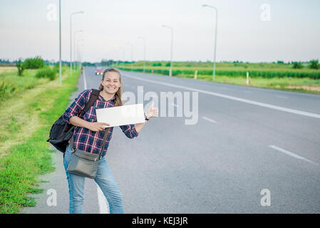 Lächelnde Frau per Anhalter auf der Straße hält ein Blank Board. Konzept: die Welt, Euro, urlaub reisen, Menschen, Urlaub. Stockfoto