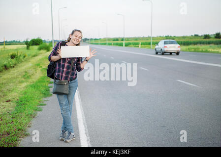 Lächelnde Frau per Anhalter auf der Straße hält ein Blank Board. Konzept: die Welt, Euro, urlaub reisen, Menschen, Urlaub. Stockfoto