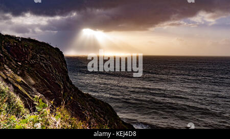 Sonnenlicht bricht durch die schweren Wolken. Dramatische Küstenansicht am frühen Morgen als der Atlantische Sturm Brian im Süden Cornwall, Großbritannien erreicht Stockfoto