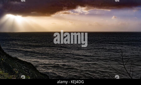 Sonnenlicht bricht durch die schweren Wolken. Dramatische Küstenansicht am frühen Morgen als der Atlantische Sturm Brian im Süden Cornwall, Großbritannien erreicht Stockfoto