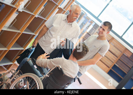 Student im Rollstuhl im Gespräch mit Mitschüler und Professor in der Bibliothek Stockfoto