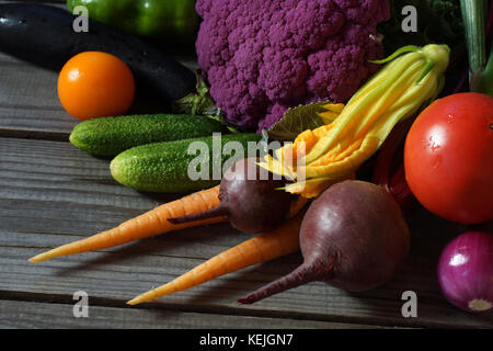 Verschiedene Gemüse liegen auf einem hölzernen Tisch: Auberginen, Paprika, Tomaten, rote Rüben, Karotten, Gurken, Zwiebeln, lila Blumenkohl, Zucchiniblüten Stockfoto