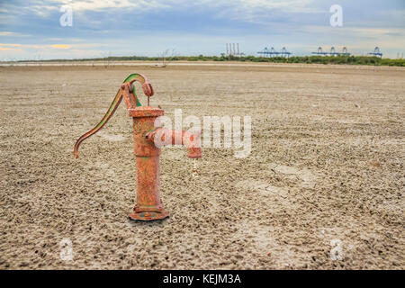 Rostiges Wasser pumpe an Land mit trockener und rissiger Boden. Wüste Stockfoto