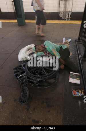 Scheinbar obdachlose Doppelamputierte schläft an ihrem zusammengebrochenen Rollstuhl auf dem U-Bahnsteig an der West 4th Street U-Bahnstation in Greenwich Village, New York City. Stockfoto