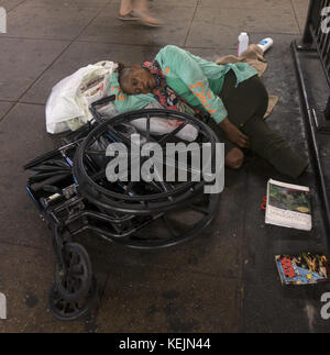 Scheinbar obdachlose Doppelamputierte schläft an ihrem zusammengebrochenen Rollstuhl auf dem U-Bahnsteig an der West 4th Street U-Bahnstation in Greenwich Village, New York City. Stockfoto