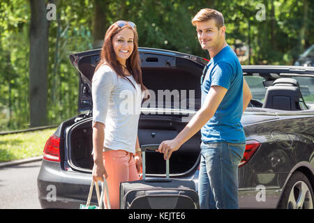 Porträt der jungen glückliches Paar, das Gepäck im Kofferraum eines Autos Stockfoto