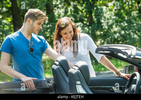 Lächelnden jungen Paar an Ihrem neu gekauften Auto suchen Stockfoto