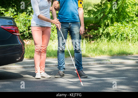 Frau Unterstützung blinder Mann mit weißem Stick auf der Straße Stockfoto